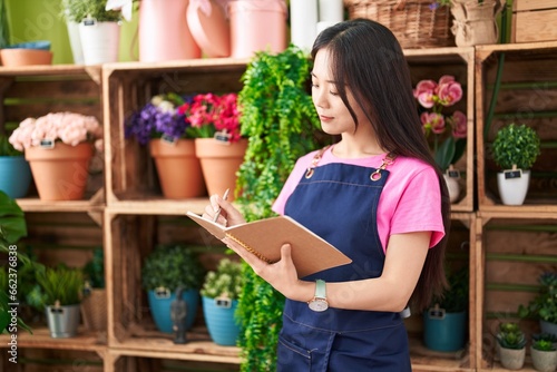 Young chinese woman florist smiling confident writing on notebook at flower shop