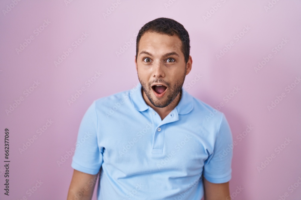 Hispanic man standing over pink background afraid and shocked with surprise and amazed expression, fear and excited face. Hispanic man standing over pink background afraid and shocked with surprise and amazed expression, fear and excited face.
