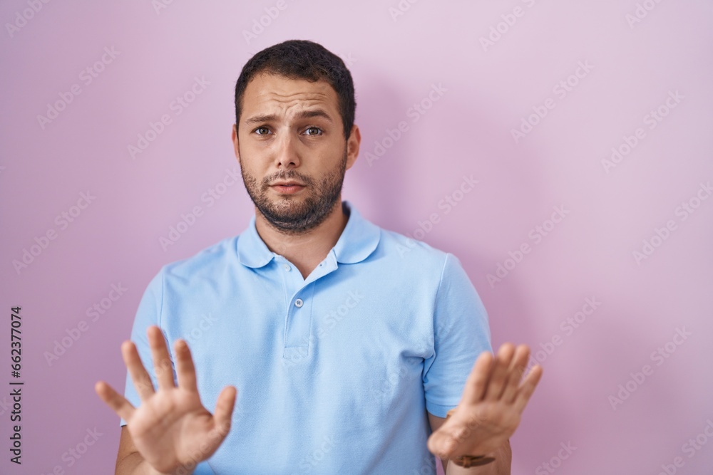 Hispanic man standing over pink background moving away hands palms showing refusal and denial with afraid and disgusting expression. stop and forbidden. Hispanic man standing over pink background moving away hands palms showing refusal and denial with afraid and disgusting expression. stop and forbidden.
