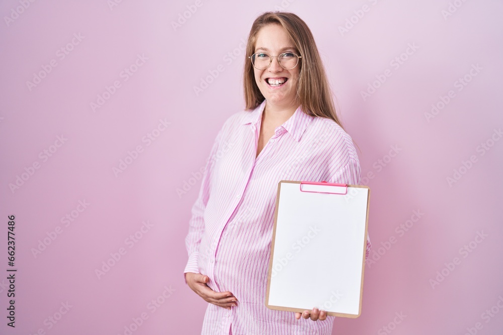 Young pregnant woman holding clipboard smiling and laughing hard out loud because funny crazy joke. Young pregnant woman holding clipboard smiling and laughing hard out loud because funny crazy joke.