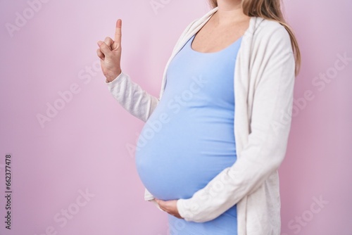 Young pregnant woman expecting a baby, touching pregnant belly smiling with an idea or question pointing finger with happy face, number one