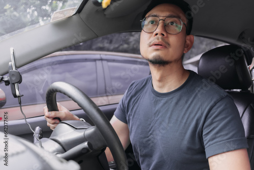 Asian Thai man with beard, wear eyeglasses and navy t-shirt, parking a car by looking at rear mirror, driving training for safety. pick up girlfriend after work.
