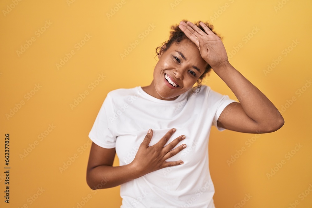 Young hispanic woman with curly hair standing over yellow background touching forehead for illness and fever, flu and cold, virus sick Young hispanic woman with curly hair standing over yellow background touching forehead for illness and fever, flu and cold, virus sick