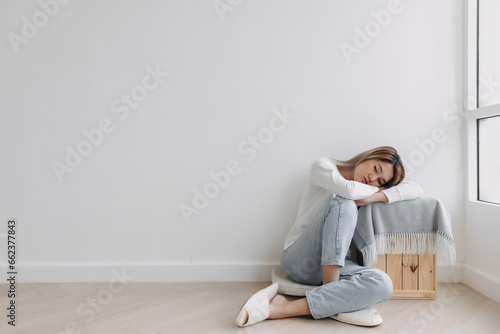 Asian Thai woman sitting on floor and resting head on arms lying on table, feeling sad and worried, thinking something lonely, absent-minded at apartment in winter. 