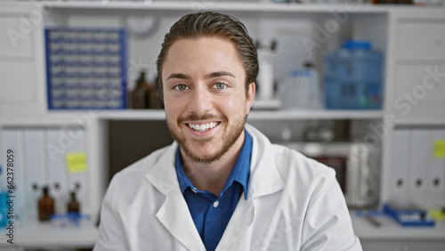 Young hispanic man scientist smiling confident sitting on chair at laboratory