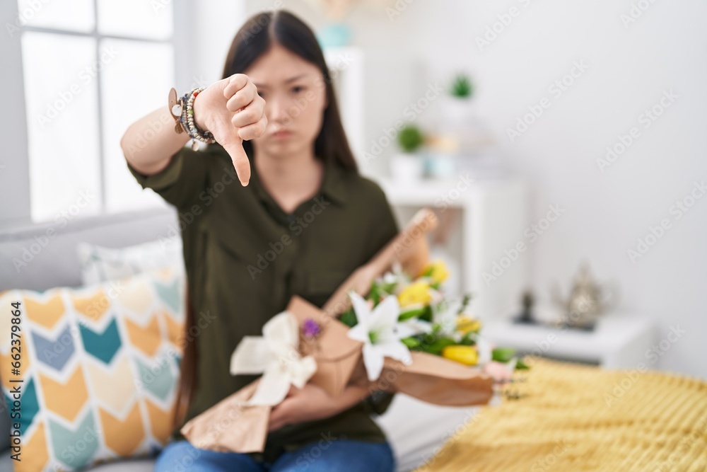 Chinese young woman holding bouquet of white flowers looking unhappy and angry showing rejection and negative with thumbs down gesture. bad expression. Chinese young woman holding bouquet of white flowers looking unhappy and angry showing rejection and negative with thumbs down gesture. bad expression.