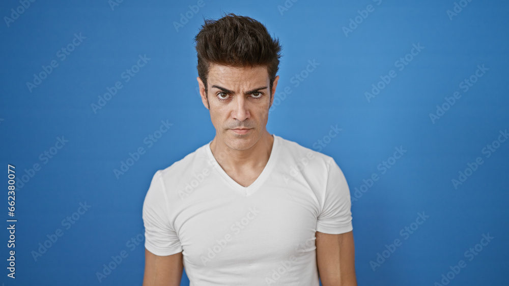 Young hispanic man standing with serious expression over isolated blue background Young hispanic man standing with serious expression over isolated blue background