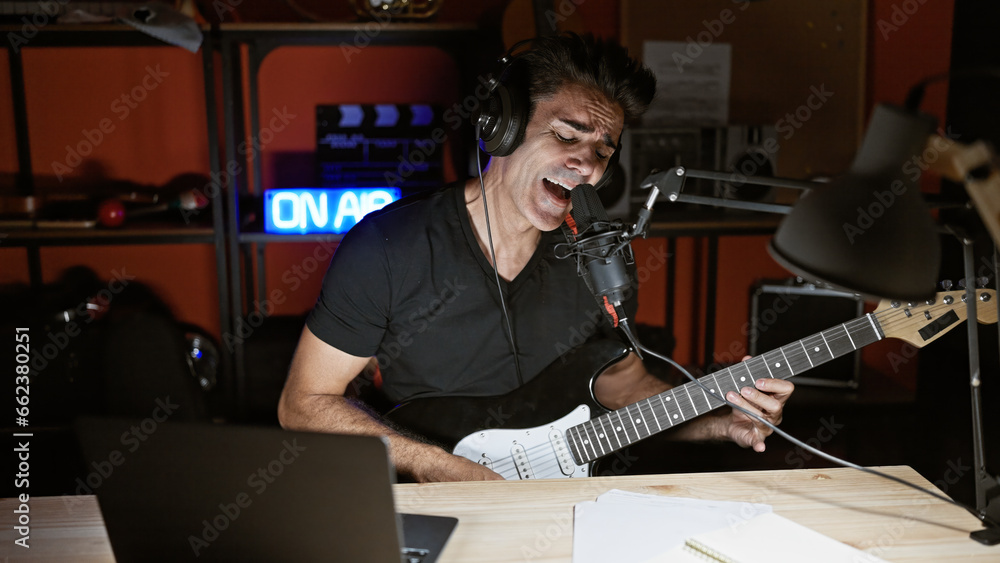 Obraz premium Young hispanic man musician singing song playing electrical guitar at radio studio