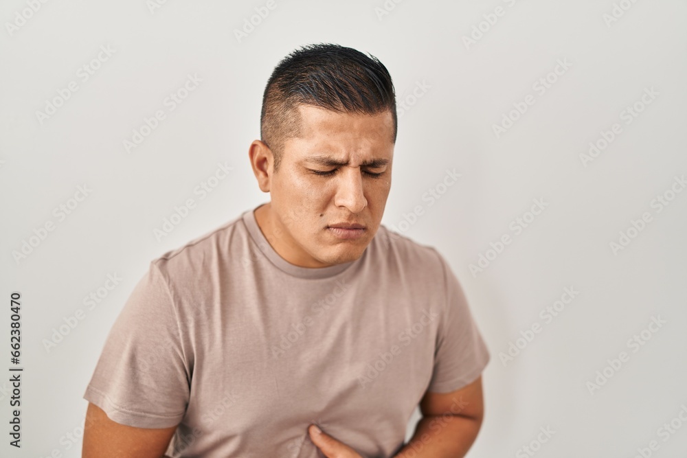 Hispanic young man standing over white background with hand on stomach because nausea, painful disease feeling unwell. ache concept. Hispanic young man standing over white background with hand on stomach because nausea, painful disease feeling unwell. ache concept.