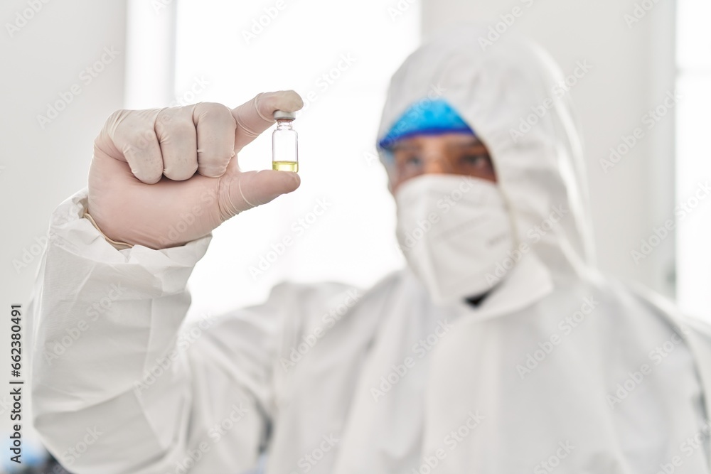 Young latin man scientist wearing covid protection uniform holding vaccine dose at laboratory Young latin man scientist wearing covid protection uniform holding vaccine dose at laboratory