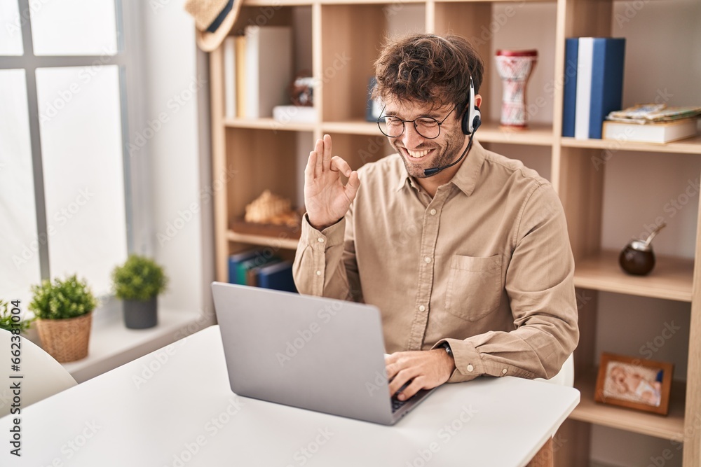 Hispanic young man wearing call center agent headset doing ok sign with fingers, smiling friendly gesturing excellent symbol Hispanic young man wearing call center agent headset doing ok sign with fingers, smiling friendly gesturing excellent symbol