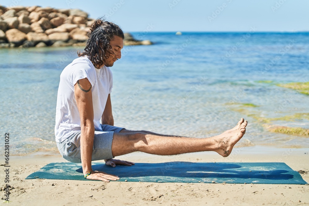 Young hispanic man doing yoga exercise sitting on sand at beach Young hispanic man doing yoga exercise sitting on sand at beach