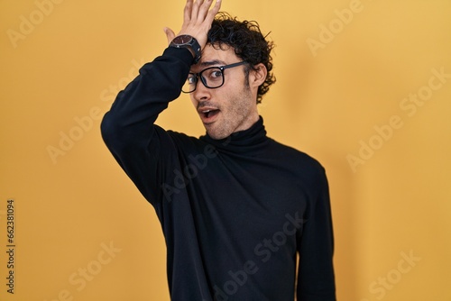 Hispanic man standing over yellow background surprised with hand on head for mistake, remember error. forgot, bad memory concept. © Krakenimages.com