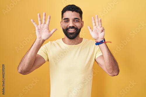 Hispanic man with beard standing over yellow background showing and pointing up with fingers number nine while smiling confident and happy.
