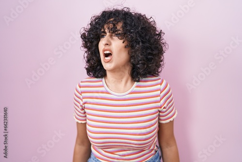 Young middle east woman standing over pink background angry and mad screaming frustrated and furious, shouting with anger. rage and aggressive concept. © Krakenimages.com