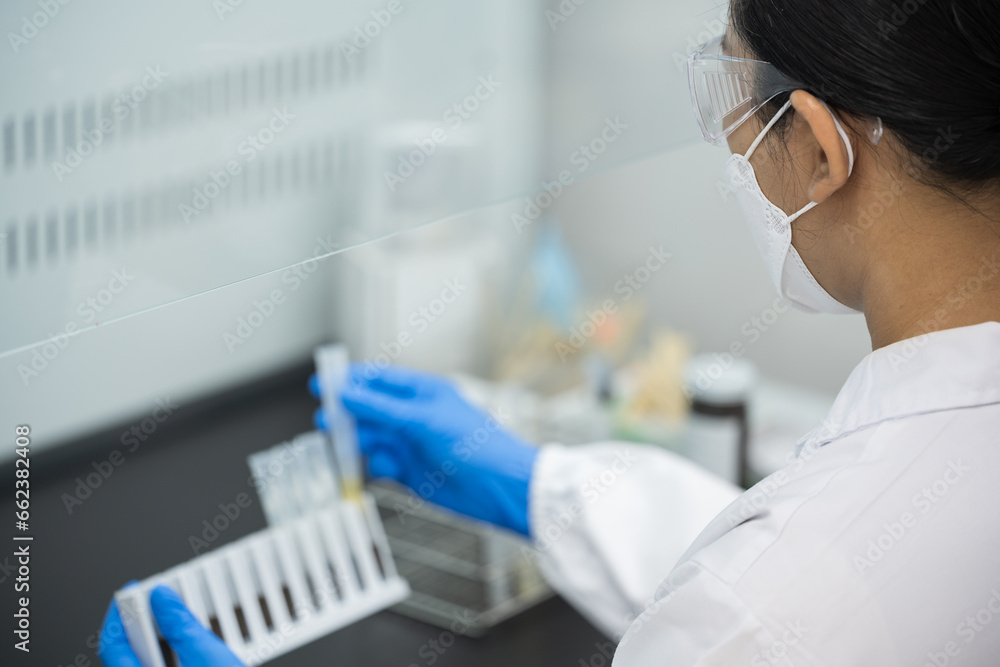 Close up scientist wearing blue gloves working with test tube in the flume hood at laboratory.Selective focus scientist hand holding sample blood test tube for fast laboratory. Close up scientist wearing blue gloves working with test tube in the flume hood at laboratory.Selective focus scientist hand holding sample blood test tube for fast laboratory.