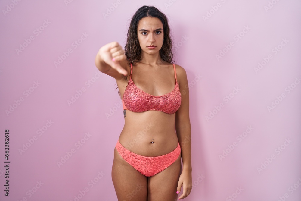 Young hispanic woman wearing lingerie over pink background looking unhappy and angry showing rejection and negative with thumbs down gesture. bad expression. - obrazy, fototapety, plakaty 