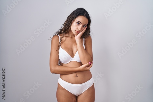 Young hispanic woman wearing white lingerie thinking looking tired and bored with depression problems with crossed arms.