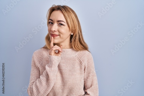Hispanic woman standing over blue background thinking concentrated about doubt with finger on chin and looking up wondering