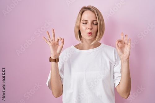 Young caucasian woman standing over pink background relaxed and smiling with eyes closed doing meditation gesture with fingers. yoga concept.