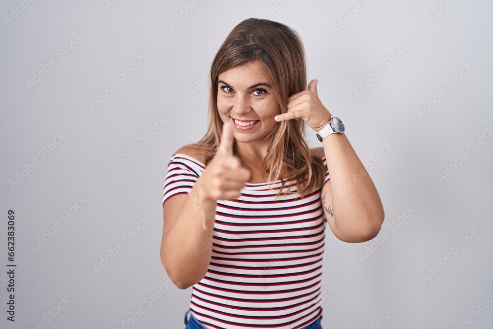 Young hispanic woman standing over isolated background smiling doing talking on the telephone gesture and pointing to you. call me. Young hispanic woman standing over isolated background smiling doing talking on the telephone gesture and pointing to you. call me.