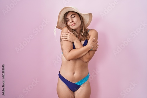 Young hispanic woman wearing bikini over pink background hugging oneself happy and positive, smiling confident. self love and self care
