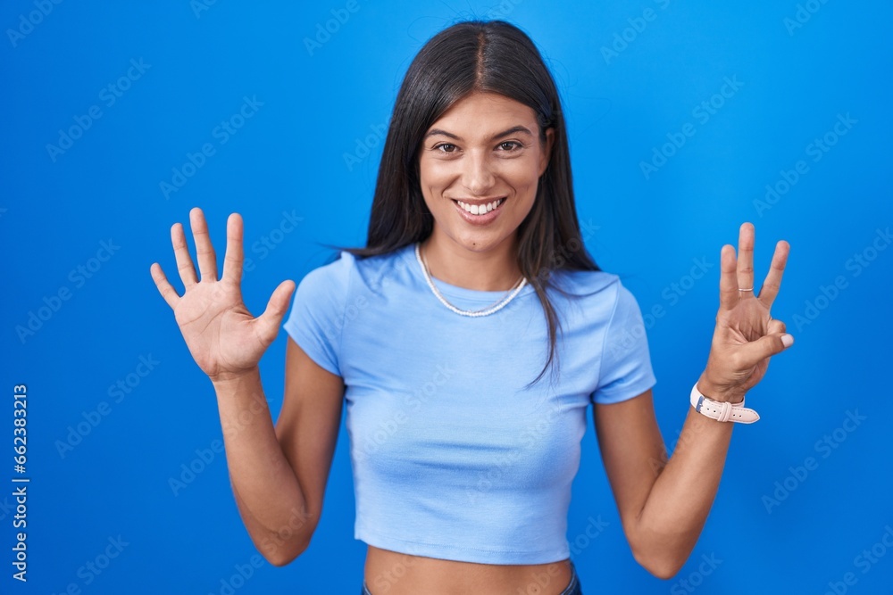 Brunette young woman standing over blue background showing and pointing up with fingers number eight while smiling confident and happy. Brunette young woman standing over blue background showing and pointing up with fingers number eight while smiling confident and happy.