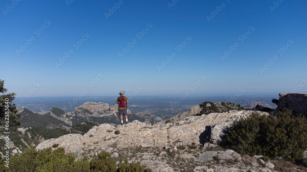 The man standing on the cliff. The hiker climbed to the rocky summit and enjoyed the views of the valley. A man looks at the clear sky in the morning sun.