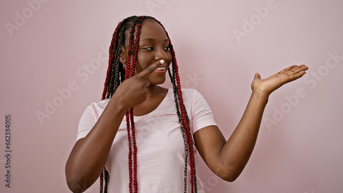 Joyful african american woman confidently presenting, pointing to the side with a beatific smile over an isolated pink background