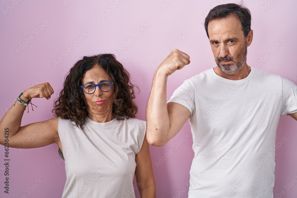 Middle age hispanic couple together over pink background showing arms muscles smiling proud. fitness concept. Middle age hispanic couple together over pink background showing arms muscles smiling proud. fitness concept.