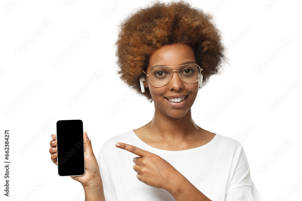 Beautiful african american woman in white t-shirt and glasses showing phone and pointing with finger at blank black screen with copy space