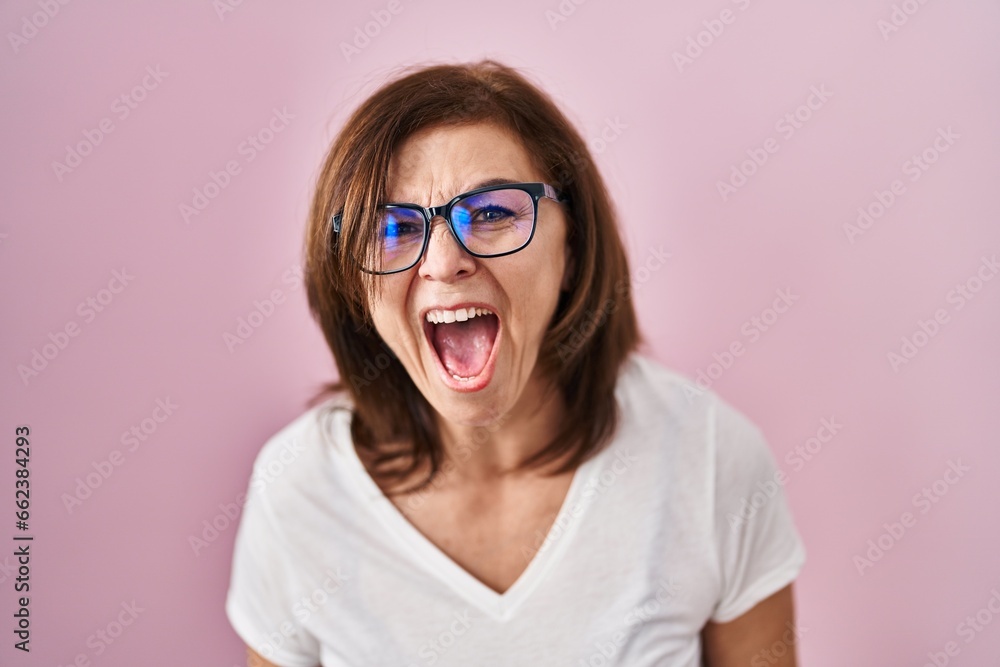 Middle age hispanic woman standing over pink background angry and mad screaming frustrated and furious, shouting with anger. rage and aggressive concept.