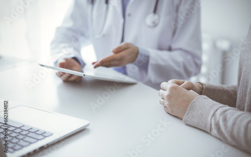 Doctor and patient sitting at the table in clinic while using tablet computer. The focus is on female patient s hands  close up. Medicine concept