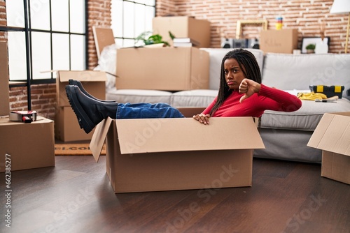 Young african american with braids moving to a new home inside of a cardboard box with angry face, negative sign showing dislike with thumbs down, rejection concept © Krakenimages.com
