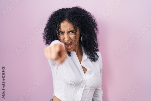 Hispanic woman with curly hair standing over pink background pointing displeased and frustrated to the camera, angry and furious with you