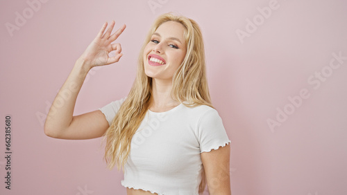 Young blonde woman smiling with ok gestur over isolated pink background