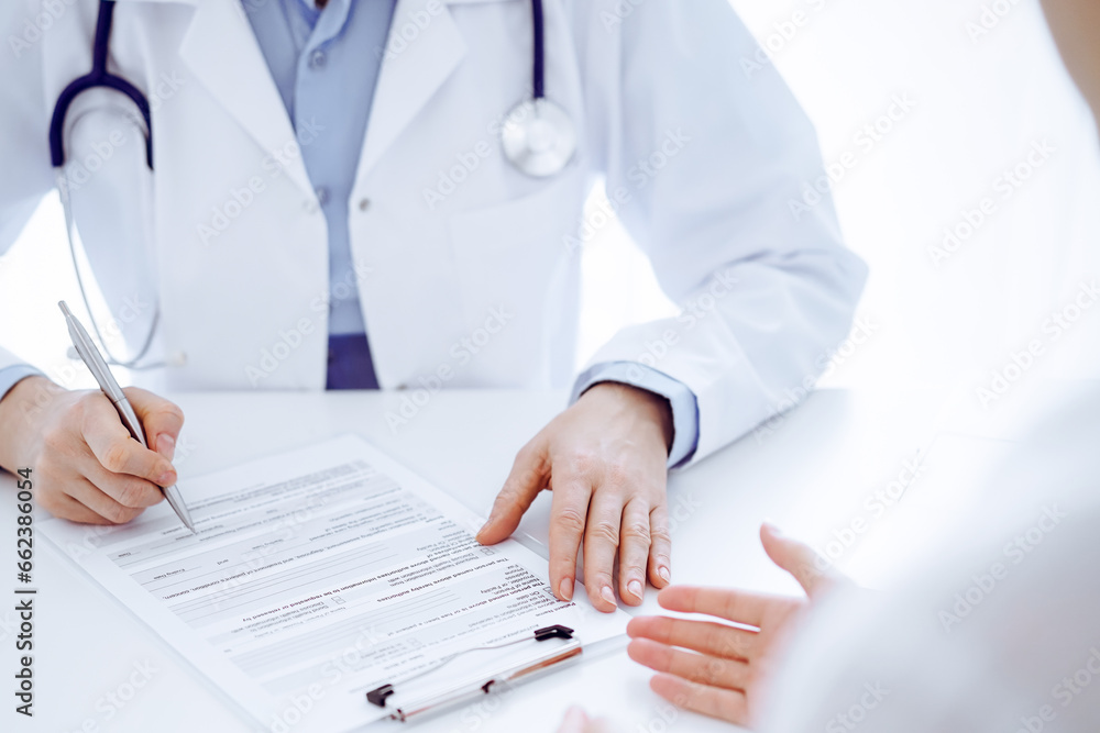 Doctor and patient discussing current health examination while sitting opposite each other at the desk in clinic. The focus is on female hands, close up. Medicine concept Doctor and patient discussing current health examination while sitting opposite each other at the desk in clinic. The focus is on female hands, close up. Medicine concept