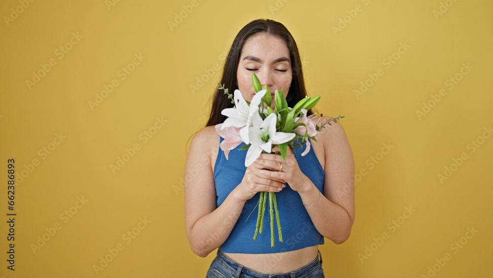 Young beautiful hispanic woman smelling bouquet of flowers over isolated yellow background Young beautiful hispanic woman smelling bouquet of flowers over isolated yellow background