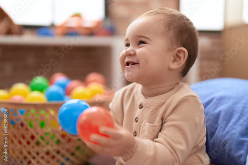 Adorable toddler playing with balls sitting on floor at kindergarten