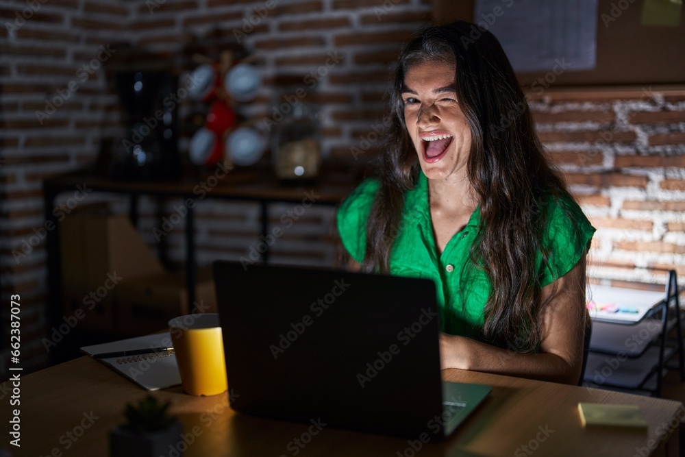 Young teenager girl working at the office at night winking looking at the camera with sexy expression, cheerful and happy face. Young teenager girl working at the office at night winking looking at the camera with sexy expression, cheerful and happy face.