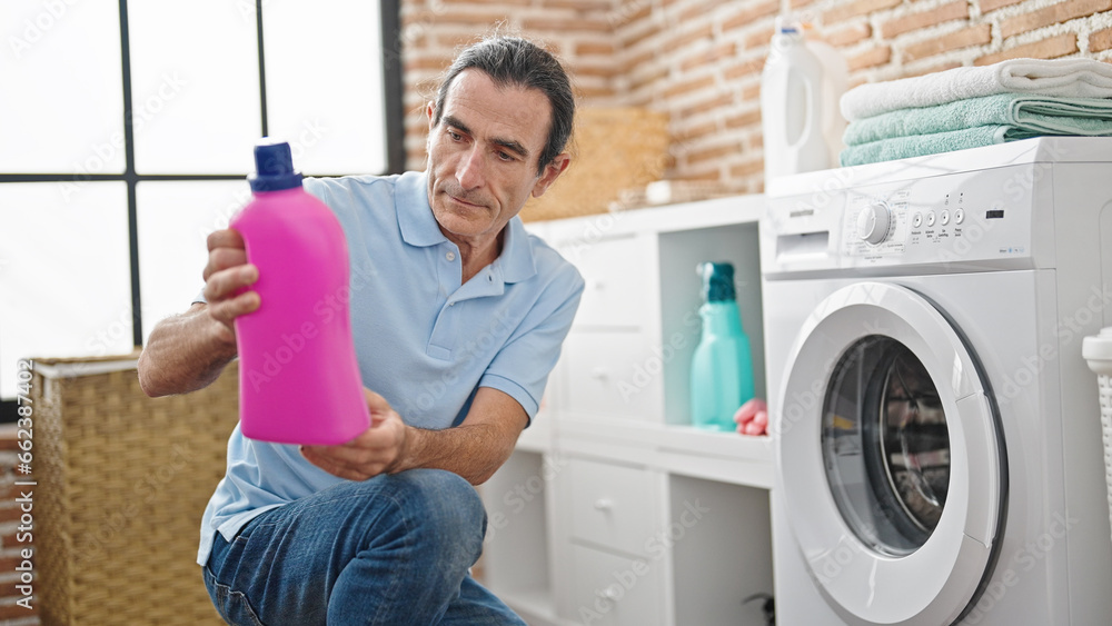 Middle age man holding detergent bottle at laundry room Middle age man holding detergent bottle at laundry room