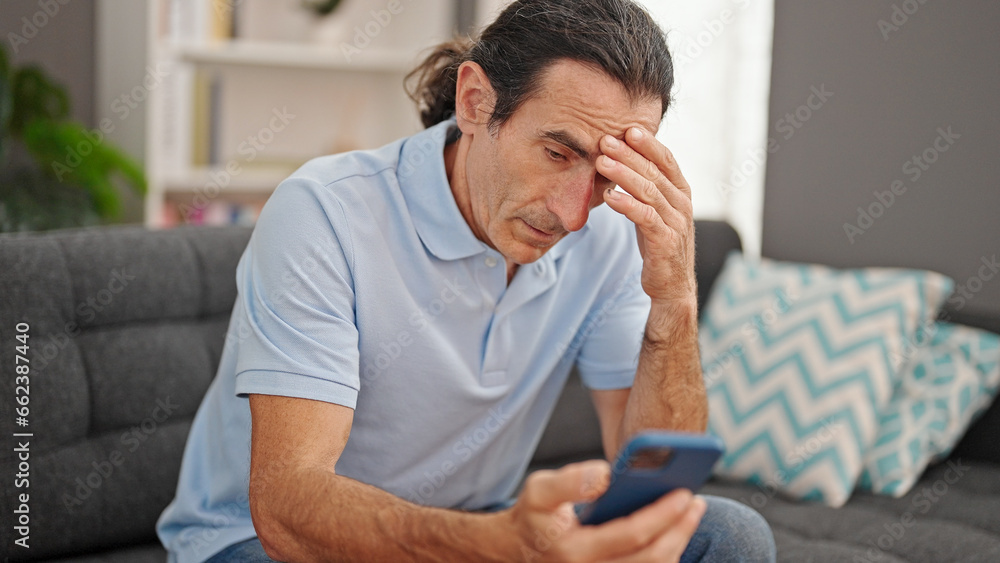 Middle age man using smartphone sitting on sofa at home Middle age man using smartphone sitting on sofa at home