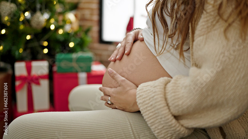 Young pregnant woman massaging belly celebrating christmas at home