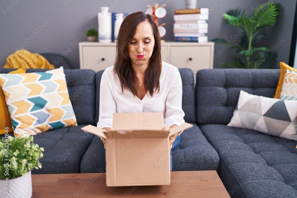 Middle age brunette woman opening cardboard box puffing cheeks with funny face. mouth inflated with air, catching air. Middle age brunette woman opening cardboard box puffing cheeks with funny face. mouth inflated with air, catching air.