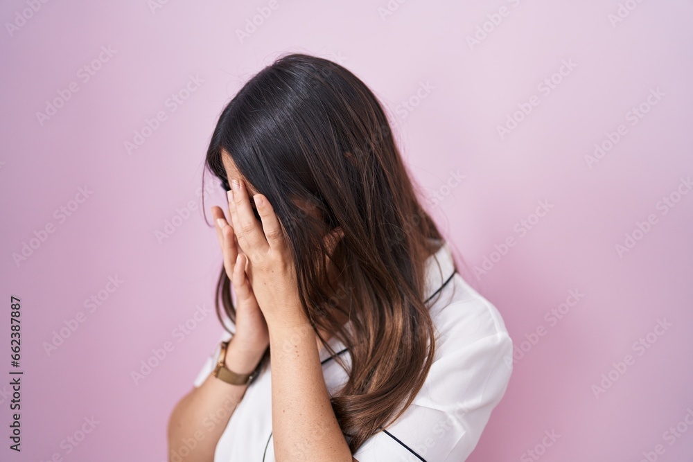 Young brunette woman wearing glasses standing over pink background with sad expression covering face with hands while crying. depression concept. Young brunette woman wearing glasses standing over pink background with sad expression covering face with hands while crying. depression concept.