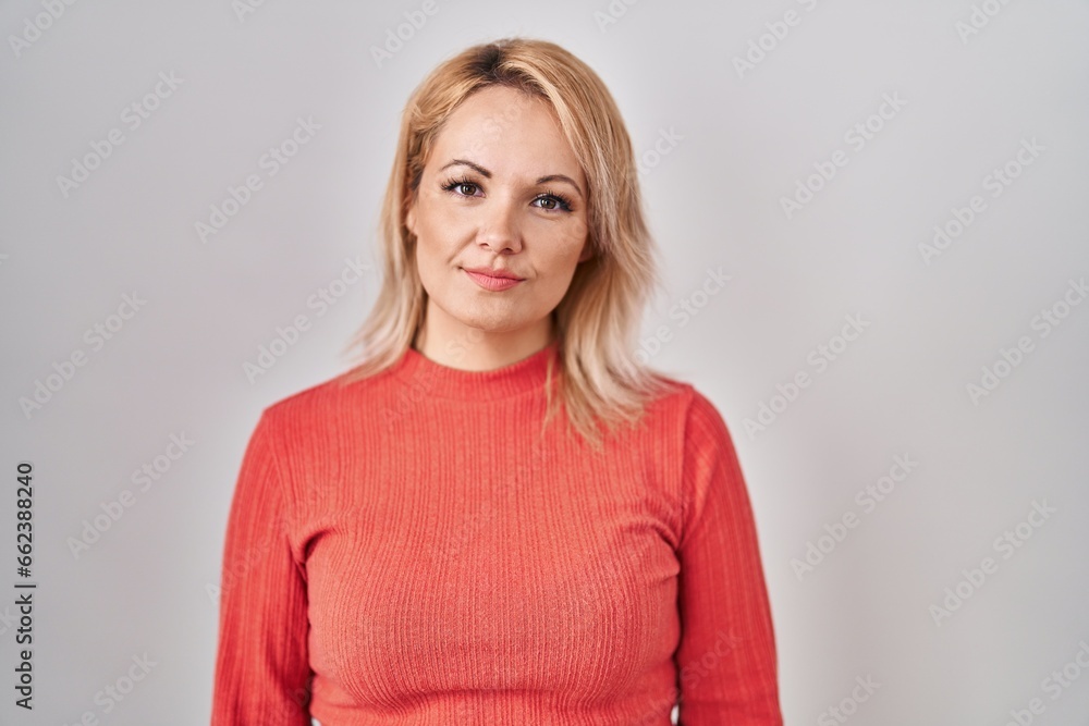 Blonde woman standing over isolated background relaxed with serious expression on face. simple and natural looking at the camera. Blonde woman standing over isolated background relaxed with serious expression on face. simple and natural looking at the camera.