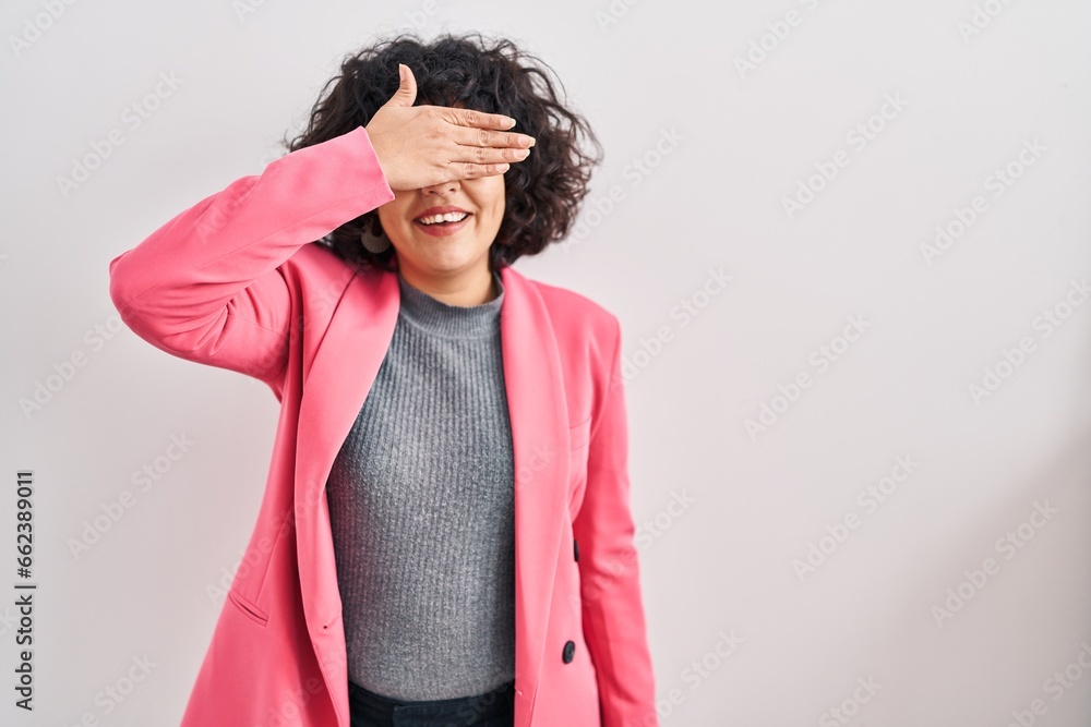 Hispanic woman with curly hair standing over isolated background smiling and laughing with hand on face covering eyes for surprise. blind concept. Hispanic woman with curly hair standing over isolated background smiling and laughing with hand on face covering eyes for surprise. blind concept.
