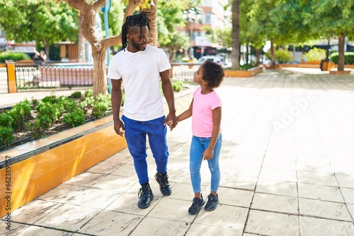 Father and daughter smiling confident walking with hands together at park
