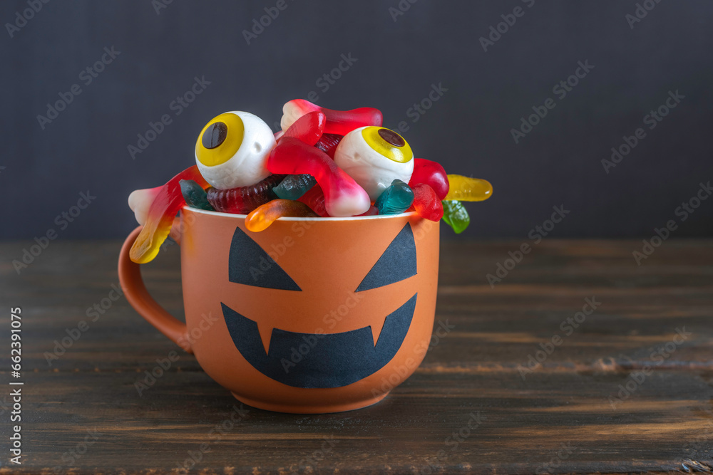Fototapeta premium Jelly worms and eyes in Halloween cup over dark wooden background.