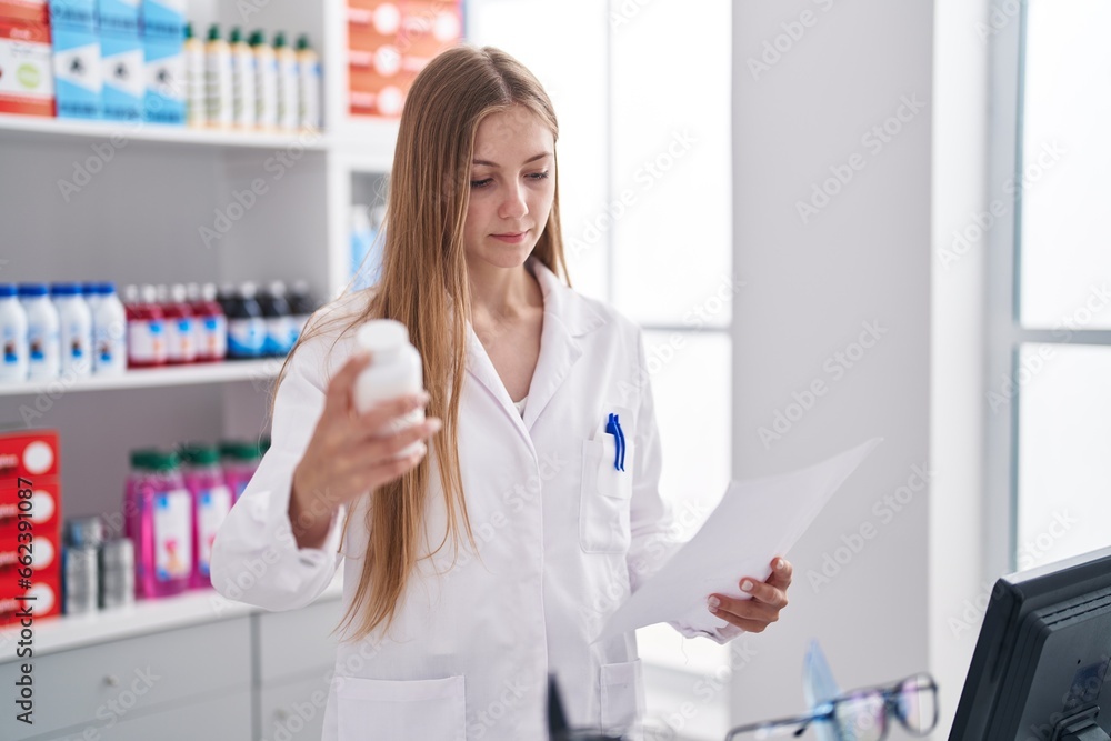 Young caucasian woman pharmacist holding pills bottle reading prescription at pharmacy